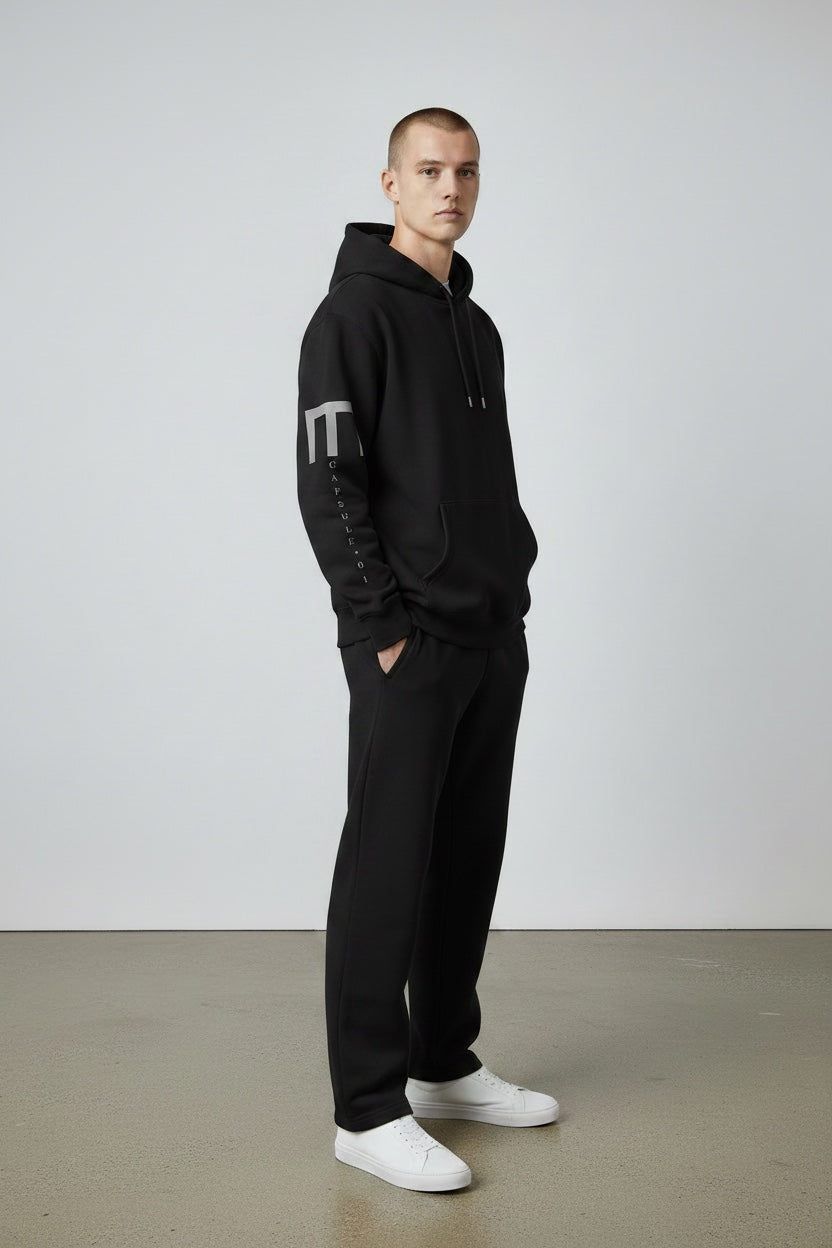 Pavel & Co black oversized hoodie with dropped shoulders and white sleeve print worn by a man with matching joggers